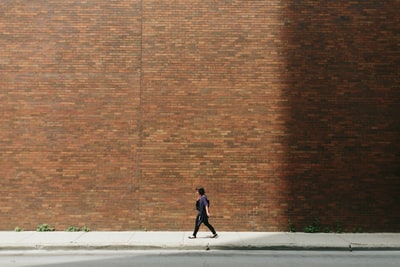 穿黑衬衫的女人走在人行道上，靠近棕色的水泥墙